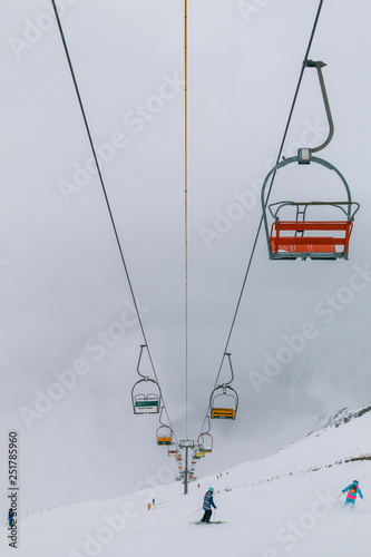 Empty old lifts for two people. Dvuhkreselny ski lift in the snow and fog. Multicolored broken gondolas in Dombai, Caucasus, Karachay-Cherkessia, Russia.