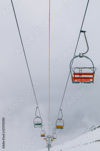 Empty old lifts for two people. Dvuhkreselny ski lift in the snow and fog. Multicolored broken gondolas in Dombai, Caucasus, Karachay-Cherkessia, Russia.