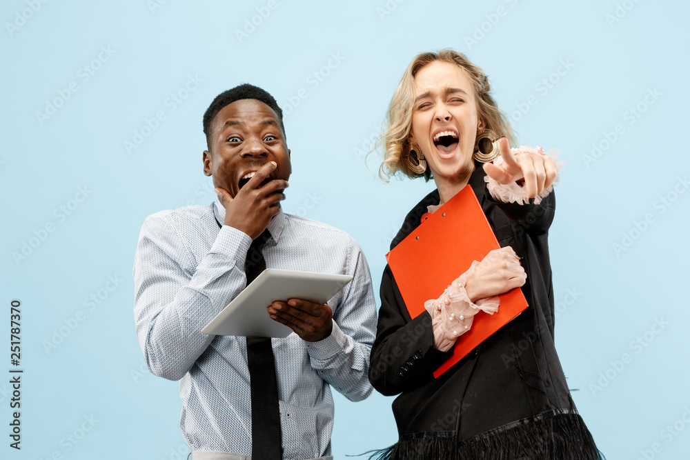Concept of partnership in business. Young happy smiling man and woman standing against blue background at studio Concept of partnership in business. Young happy smiling man and woman standing against blue background at studio