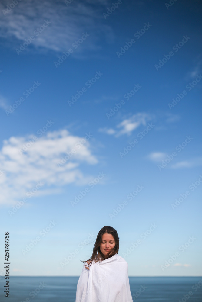 Beautiful dark hair young white european woman wrapped in white cloth sheet. In a blue sky background. Shot on Parnidis dune in Nida, Lithuania, in Curonian Spit. Sunny day with blue sky.