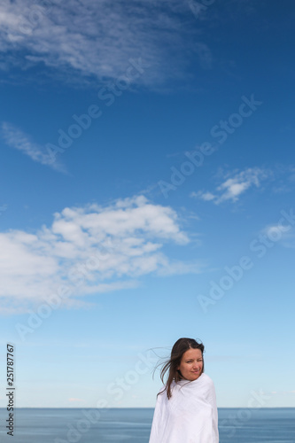 Beautiful dark hair young white european woman wrapped in white cloth sheet. In a blue sky background. Shot on Parnidis dune in Nida, Lithuania, in Curonian Spit. Sunny day with blue sky.