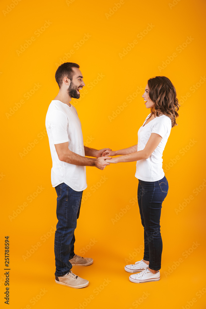 Full length photo of beautiful couple laughing and holding hands, isolated over yellow background