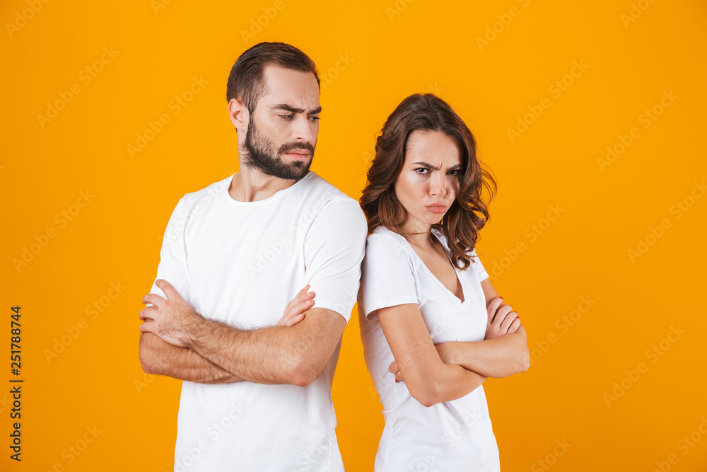 Photo of discontent man and woman in quarrel standing back to back with arms folded, isolated over yellow background Photo of discontent man and woman in quarrel standing back to back with arms folded, isolated over yellow background