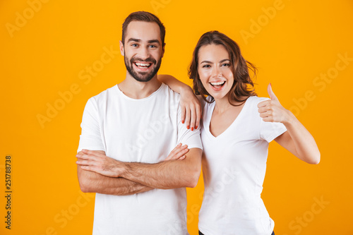 Image of cheerful people man and woman in basic clothing smiling, while standing together isolated over yellow background
