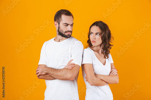 Photo of unhappy man and woman in quarrel standing back to back with arms folded, isolated over yellow background photo
