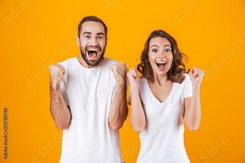 Image of ecstatic people man and woman in basic clothing laughing, while standing together isolated over yellow background