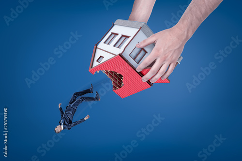 Close-up of man's hands holding house with hole in roof upside down and dropping out little businessman. photo
