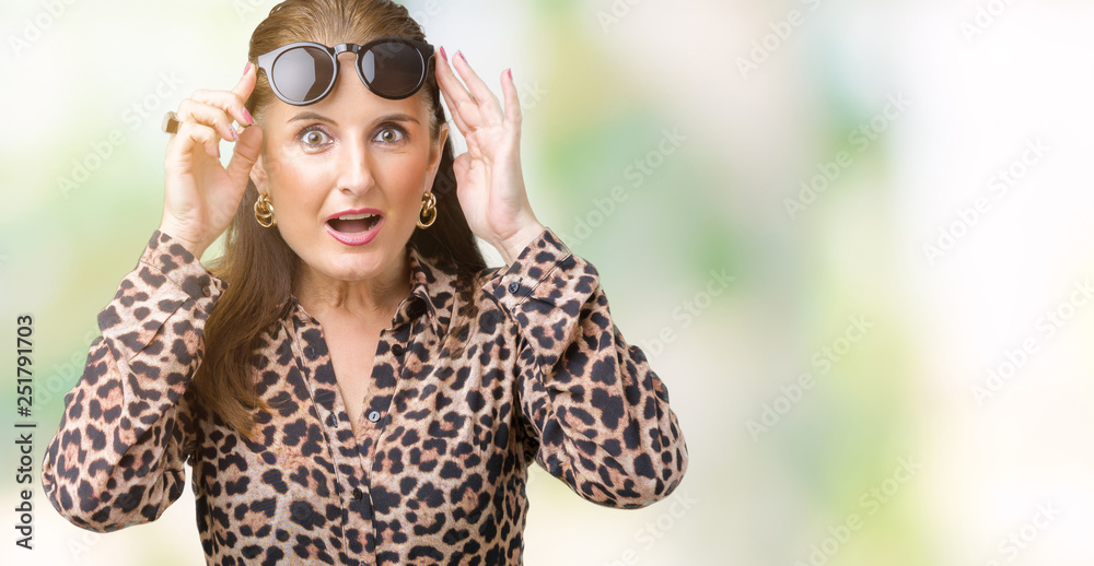 Middle age mature rich woman wearing sunglasses and leopard dress over isolated background afraid and shocked with surprise expression, fear and excited face. Middle age mature rich woman wearing sunglasses and leopard dress over isolated background afraid and shocked with surprise expression, fear and excited face.