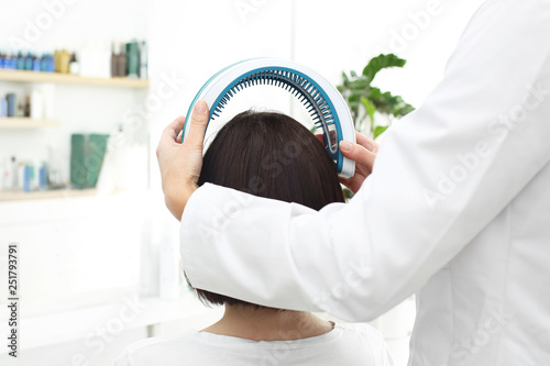 Laseroterapia skóry głowy i włosów. Kobieta z cienkimi  i słabymi włosami podczas zabiegu w gabinecie lekarskim.