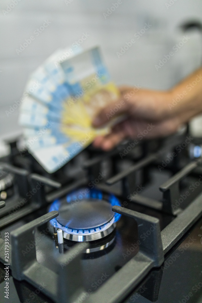 Obraz premium Cooktop with burning gas ring with hands holding money 9 uah hryvnas for combustion at home.