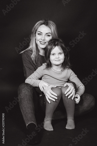 Black and white photo of mom and daughter in studio. Balck background