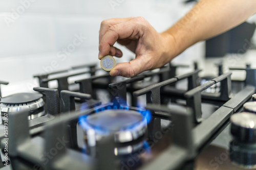 Cooktop with burning gas ring with hands holding coin of 1 euro for combustion at home.