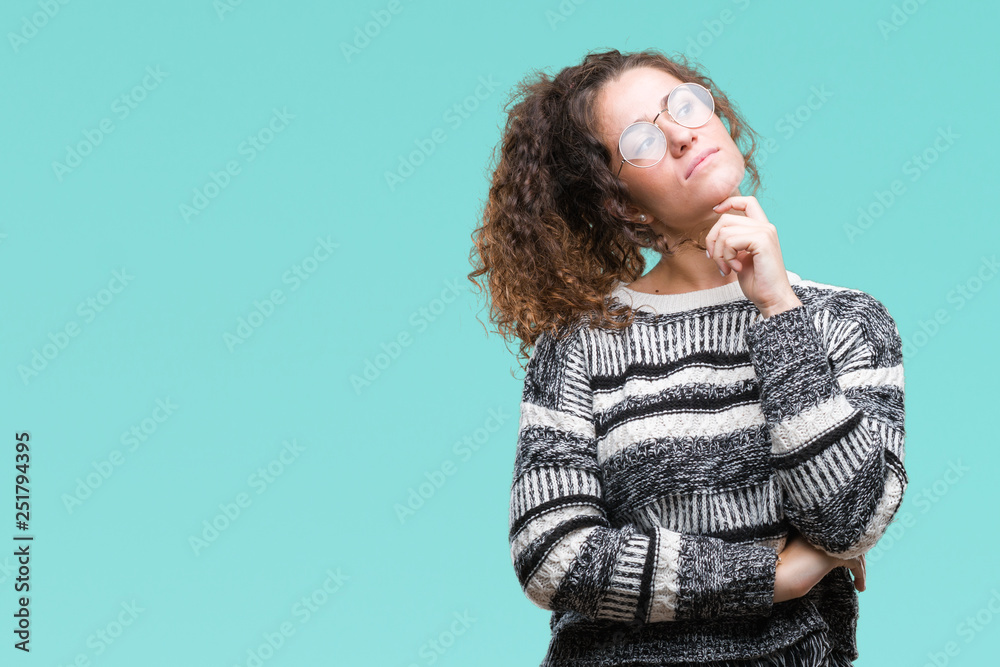 Beautiful brunette curly hair young girl wearing glasses over isolated background with hand on chin thinking about question, pensive expression. Smiling with thoughtful face. Doubt concept. Beautiful brunette curly hair young girl wearing glasses over isolated background with hand on chin thinking about question, pensive expression. Smiling with thoughtful face. Doubt concept.