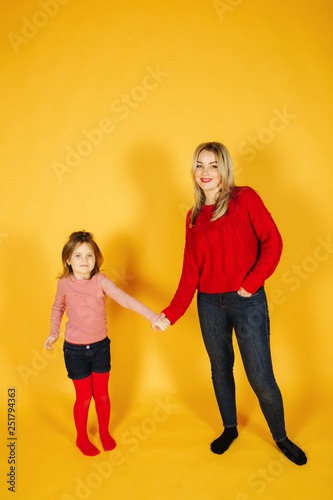 Mom and daughter standing on the yellow background in studio