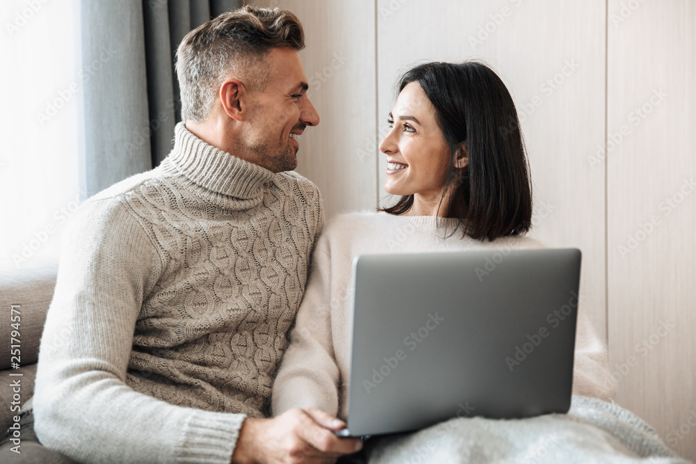 Happy loving couple family sitting on sofa indoors on sofa using laptop computer. Happy loving couple family sitting on sofa indoors on sofa using laptop computer.