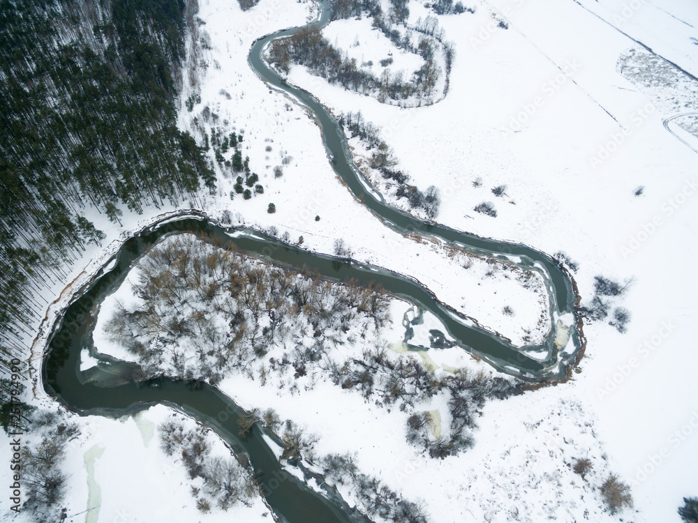 Winter landscape on the river with a forest among snow with a bird's-eye view. Drone view photo from the drone on a cloudy day. Aerial top view beautiful snowy landscape