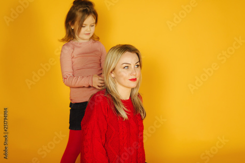 Happy little daughter braids mom's pigtail on yellow background. weaves a pigtail for mom
