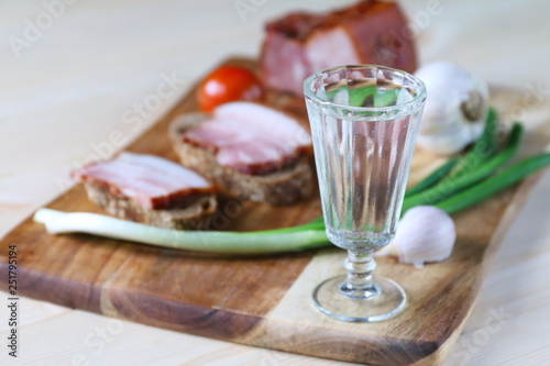 A glass of vodka is on a cutting board with a pieces of lard.