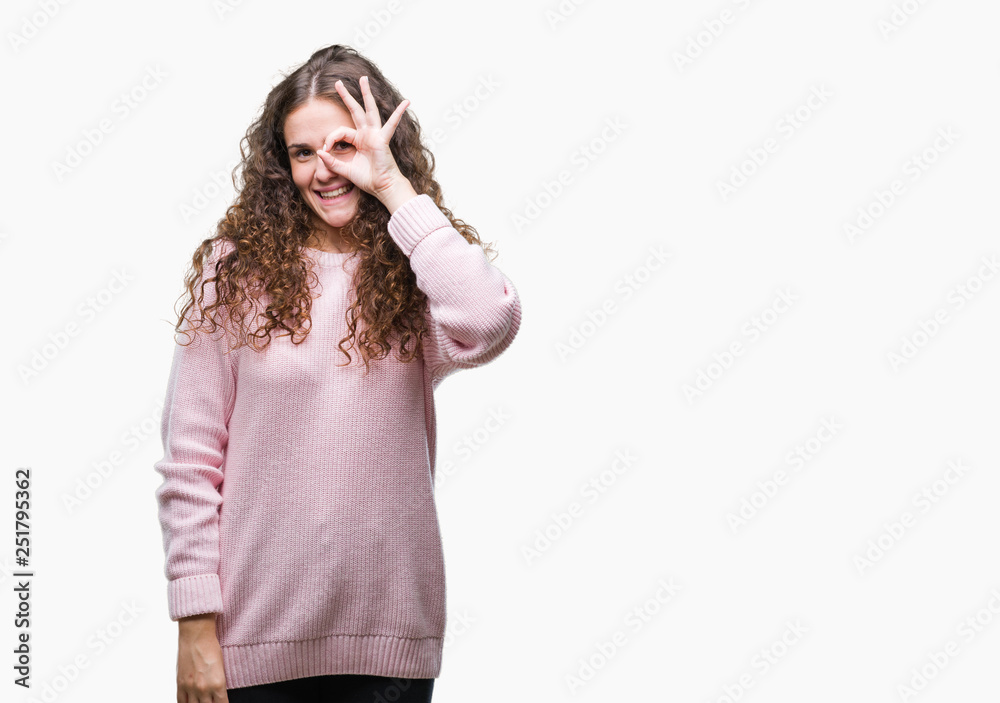 Beautiful brunette curly hair young girl wearing pink winter sweater over isolated background doing ok gesture with hand smiling, eye looking through fingers with happy face. Beautiful brunette curly hair young girl wearing pink winter sweater over isolated background doing ok gesture with hand smiling, eye looking through fingers with happy face.
