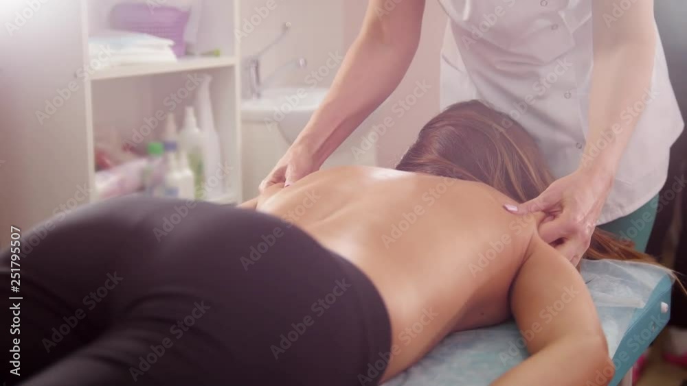 Beauty clinic. A young brunette woman receiving a back and hands massage. View from behind Beauty clinic. A young brunette woman receiving a back and hands massage. View from behind