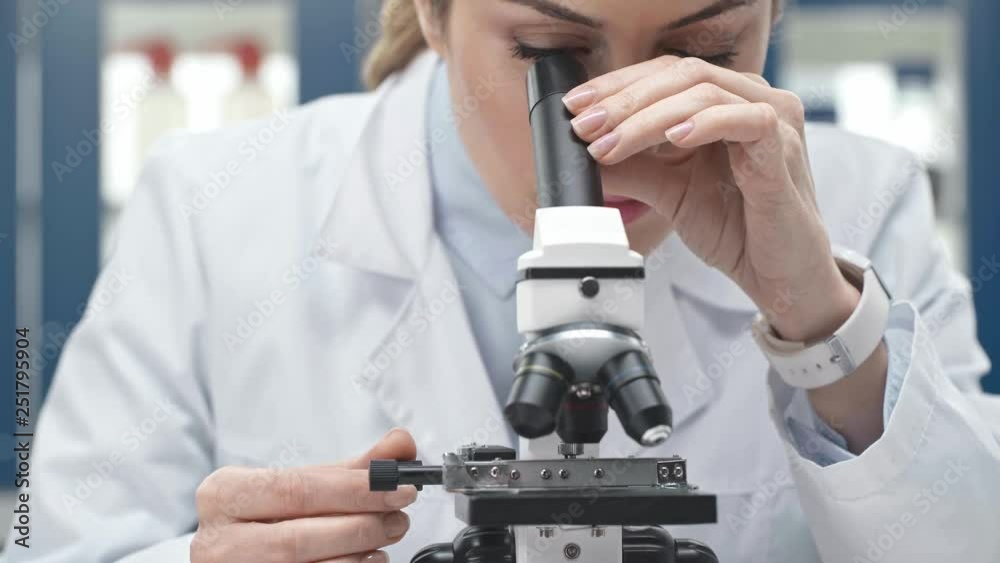 female scientist in white coat looking through microscope in laboratory female scientist in white coat looking through microscope in laboratory