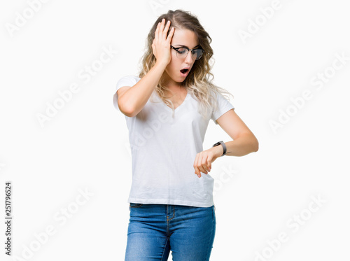 Beautiful young blonde woman wearing glasses over isolated background Looking at the watch time worried, afraid of getting late
