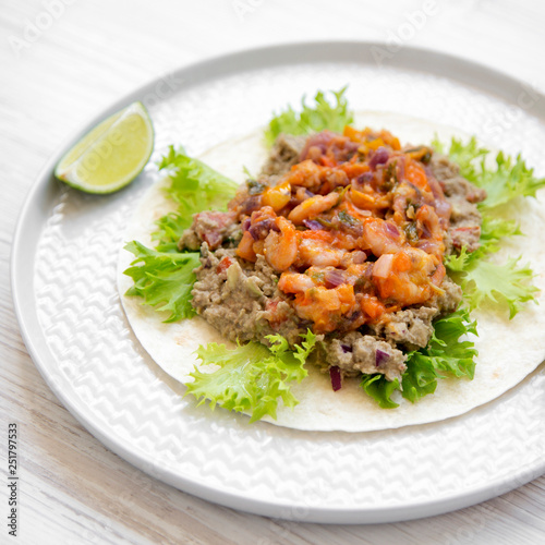 Shrimp taco with lime on round plate over white wooden background, side view. Closeup.
