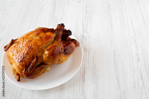 Homemade tasty rotisserie chicken on white plate over white wooden background, low angle view. Copy space. photo