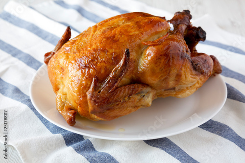 Homemade rotisserie chicken on white plate, side view. Close-up. photo