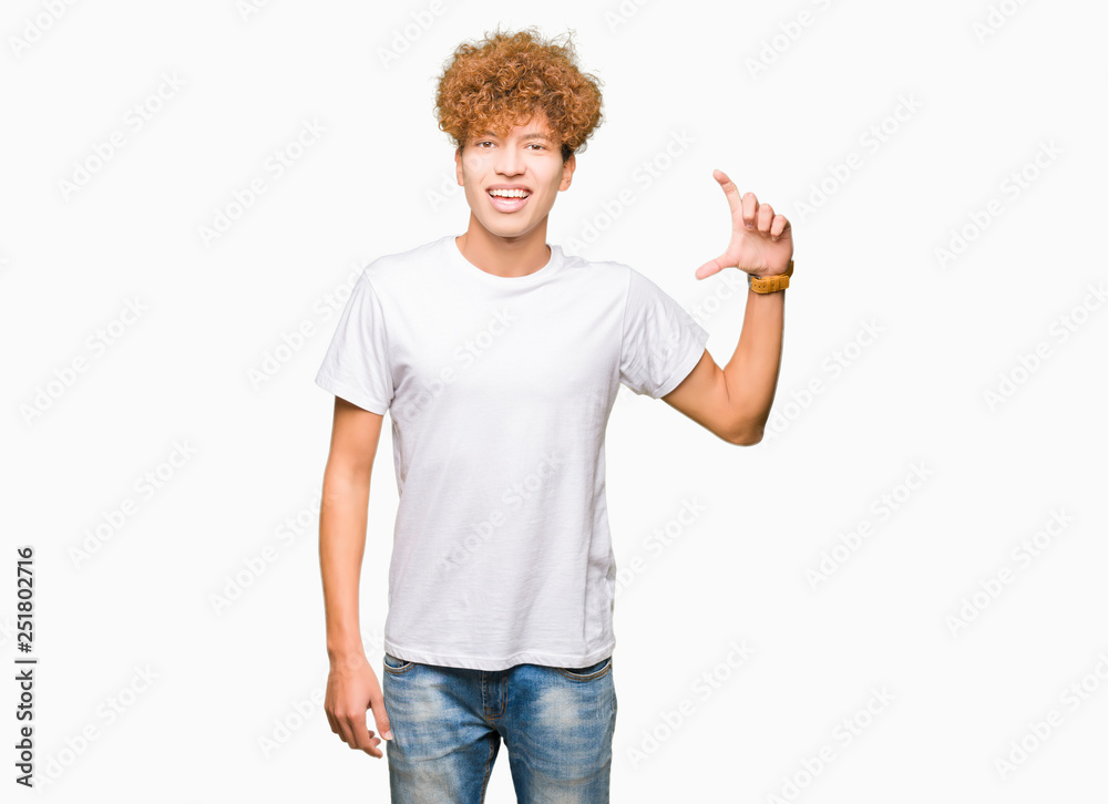 Young handsome man with afro hair wearing casual white t-shirt smiling and confident gesturing with hand doing size sign with fingers while looking and the camera. Measure concept. Young handsome man with afro hair wearing casual white t-shirt smiling and confident gesturing with hand doing size sign with fingers while looking and the camera. Measure concept.
