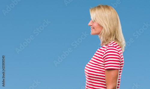 Middle age blonde woman over isolated background looking to side, relax profile pose with natural face with confident smile.