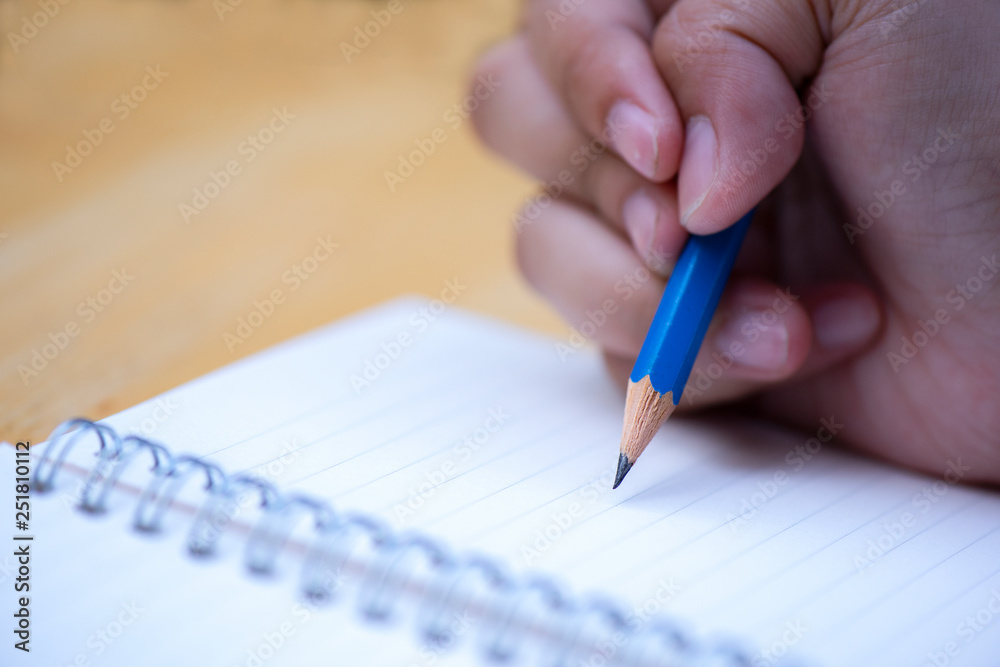 Close up hand holding pen writing notebook on wood background Close up hand holding pen writing notebook on wood background