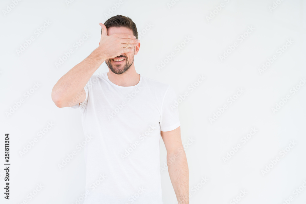 Young handsome man wearing casual white t-shirt over isolated background smiling and laughing with hand on face covering eyes for surprise. Blind concept. Young handsome man wearing casual white t-shirt over isolated background smiling and laughing with hand on face covering eyes for surprise. Blind concept.