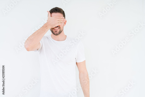 Young handsome man wearing casual white t-shirt over isolated background smiling and laughing with hand on face covering eyes for surprise. Blind concept.