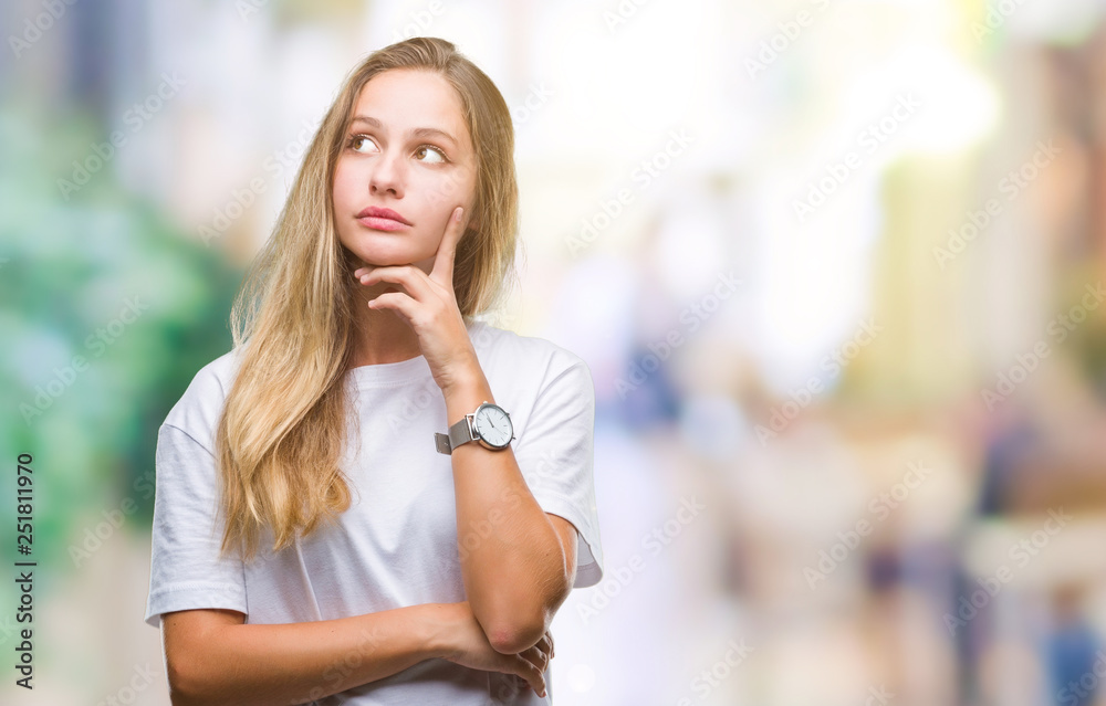 Young beautiful blonde woman wearing casual white t-shirt over isolated background with hand on chin thinking about question, pensive expression. Smiling with thoughtful face. Doubt concept.