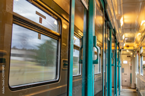 The corridor of wagon with reflection of surroundings in door glass. The interior of moving train with long corridor and doors and windows.