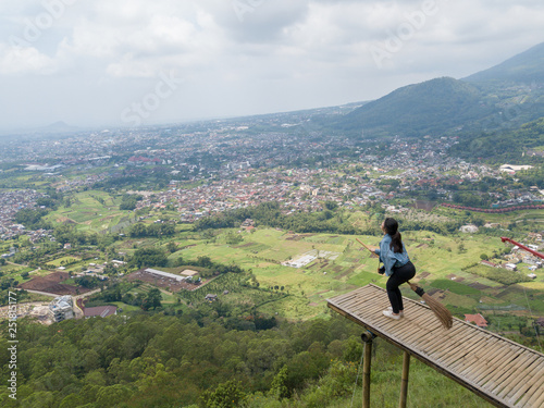 Girl hold broom in Area of Place name Omah Kayu, top hill in Batu Malang, Indonesia with tree house building by high tree and adventure traveler visit.