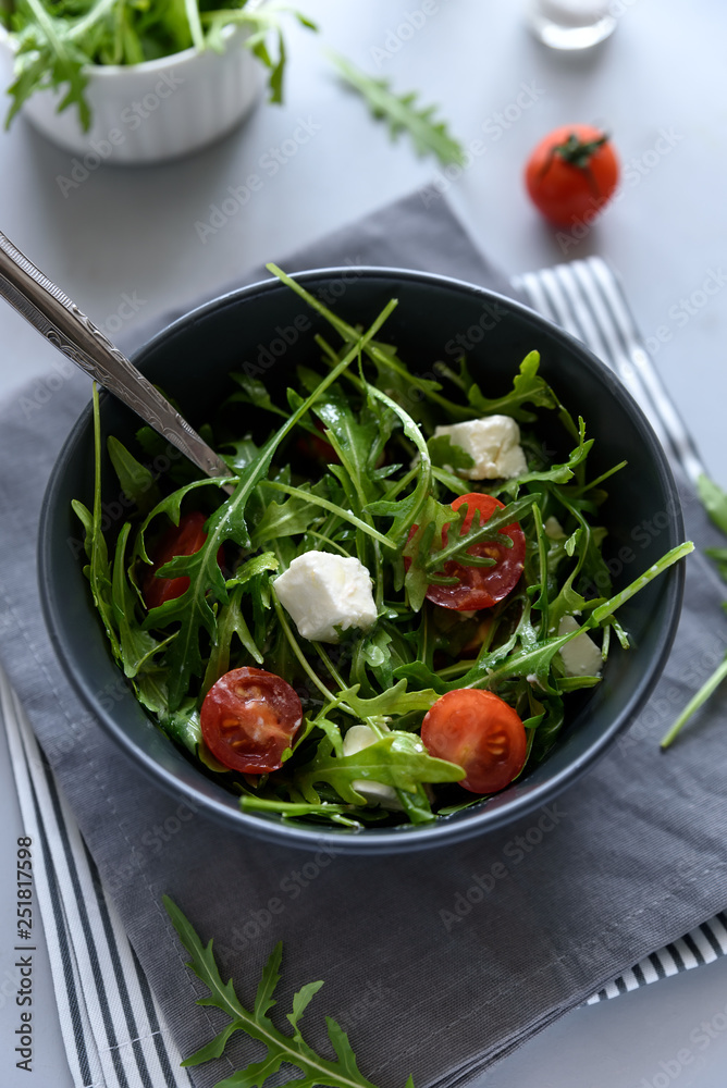 Bowl of arugula salad with tomatoes and cheese on gray wooden background. Vegetarian food concept Bowl of arugula salad with tomatoes and cheese on gray wooden background. Vegetarian food concept