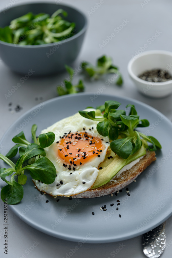 Toast (sandwich) with cream cheese, avocado, fried egg and greens on gray wooden background. Selective focus. Healthy eating or vegetarian food concept Toast (sandwich) with cream cheese, avocado, fried egg and greens on gray wooden background. Selective focus. Healthy eating or vegetarian food concept