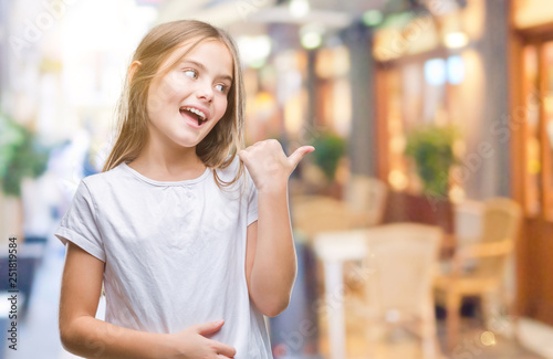 Young beautiful girl over isolated background smiling with happy face looking and pointing to the side with thumb up.