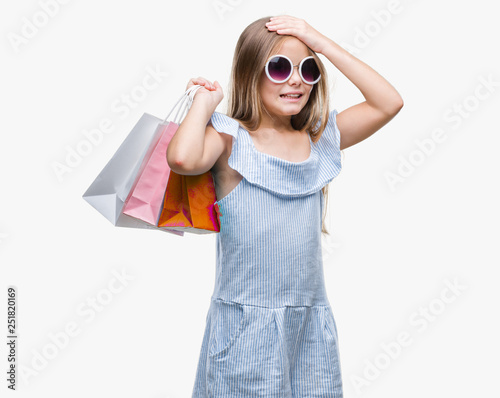 Young beautiful girl holding shopping bags on sales over isolated background stressed with hand on head, shocked with shame and surprise face, angry and frustrated. Fear and upset for mistake.