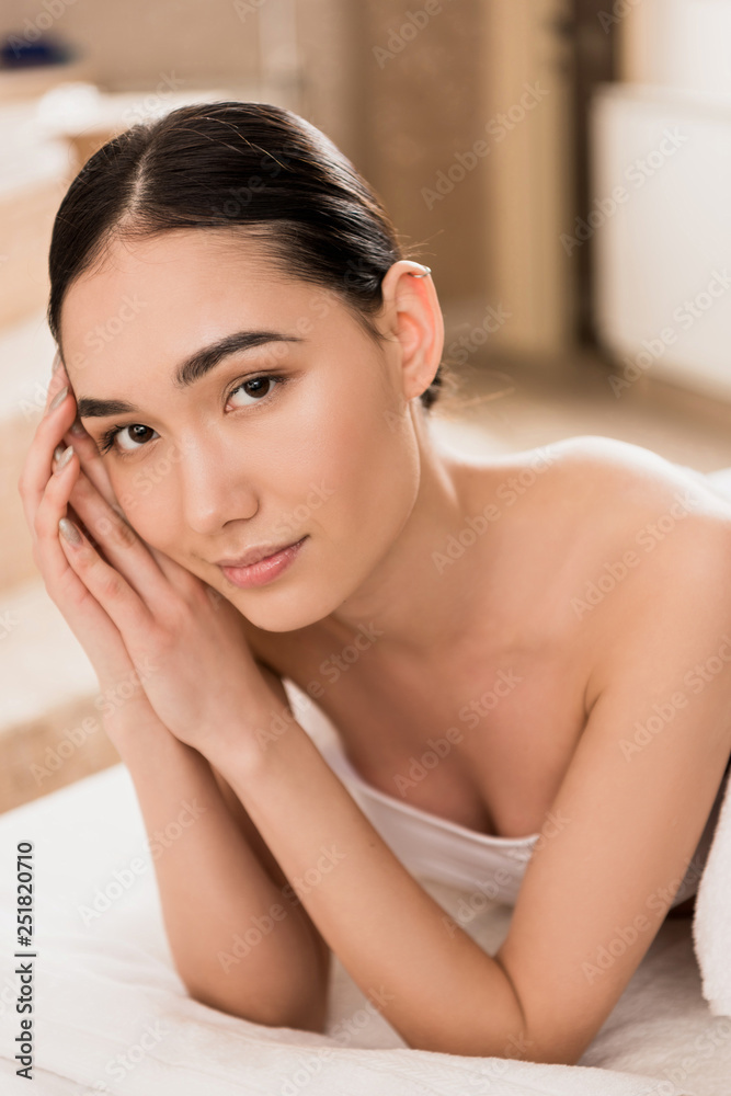 beautiful asian woman in towel lying and looking at camera at spa beautiful asian woman in towel lying and looking at camera at spa