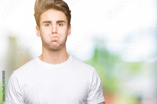Young handsome man wearing white t-shirt over isolated background puffing cheeks with funny face. Mouth inflated with air, crazy expression.