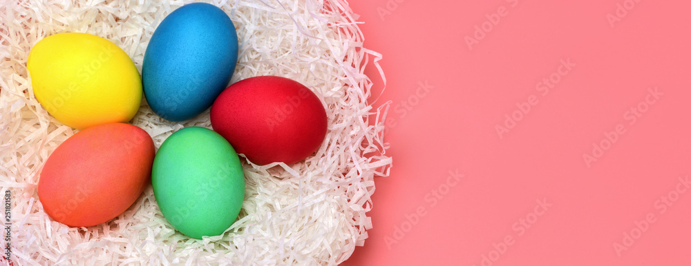 Banner. Five Easter eggs lie in a white nest on a gently pink background. Elongated photo Banner. Five Easter eggs lie in a white nest on a gently pink background. Elongated photo