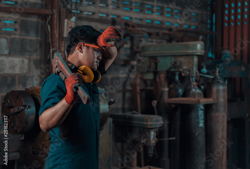 Mechanical engineer taking a break and wiping sweat off his forehead while resting a pipe wrench on his shoulder during his work shift