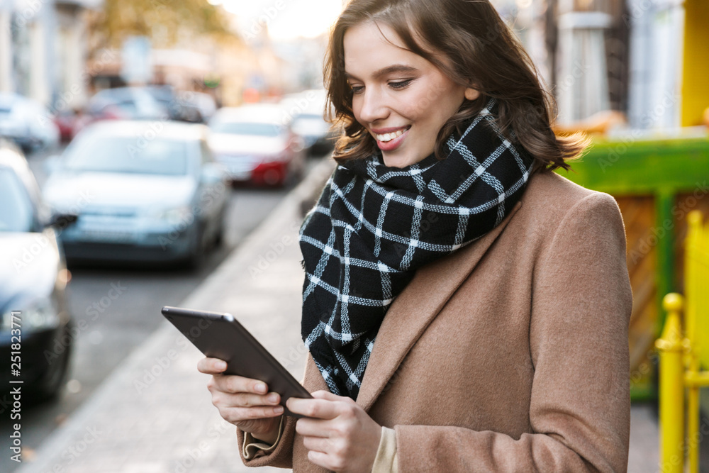 Beautiful happy young woman using tablet computer outdoors walking by street. Beautiful happy young woman using tablet computer outdoors walking by street.