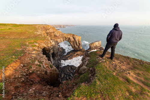 Man hiking and looking at The Green Bridge of Wales, Pembrokeshire Coast, West Wales, UK