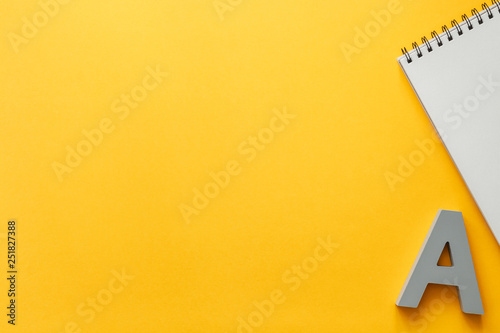 Yellow empty background with space for text. Copy space. Creative concept desk. Top view. Opened notebook and gray letter A.