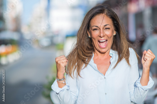 Beautiful middle age hispanic woman at the city street on a sunny day screaming proud and celebrating victory and success very excited, cheering emotion
