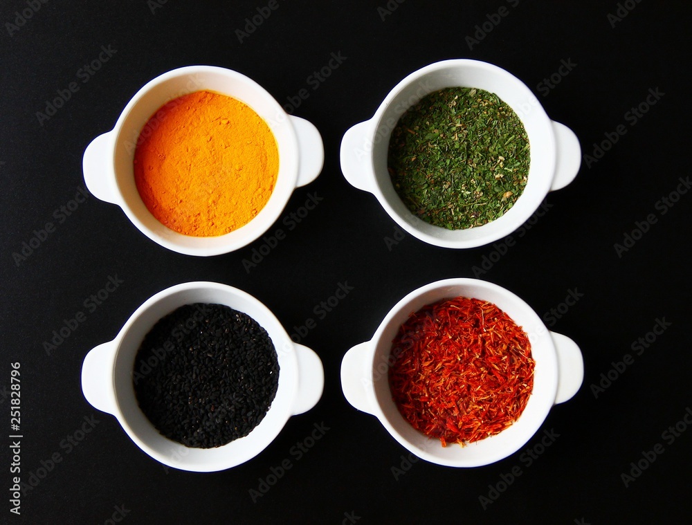Four plates with seasonings and spices are on a dark background.